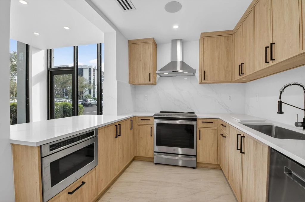 Completed custom Boca West kitchen with warm wood-toned cabinetry, pale countertops and black cabinet hardware